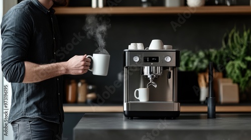Man holding a mug and standing next to a coffee machine in a modern kitchen waiting for the coffee to pour