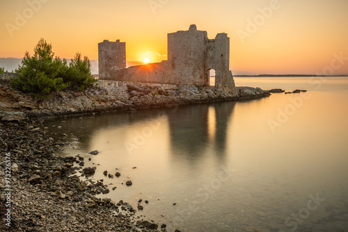 Castle ruins at dawn. Bay on the Mediterranean Sea with calm water at sunrise. Reflection of the sky and Mediterranean landscape of Kastelina Castle, Vir Island, Zadar, Dalmatia, Croatia, Adriatic Sea