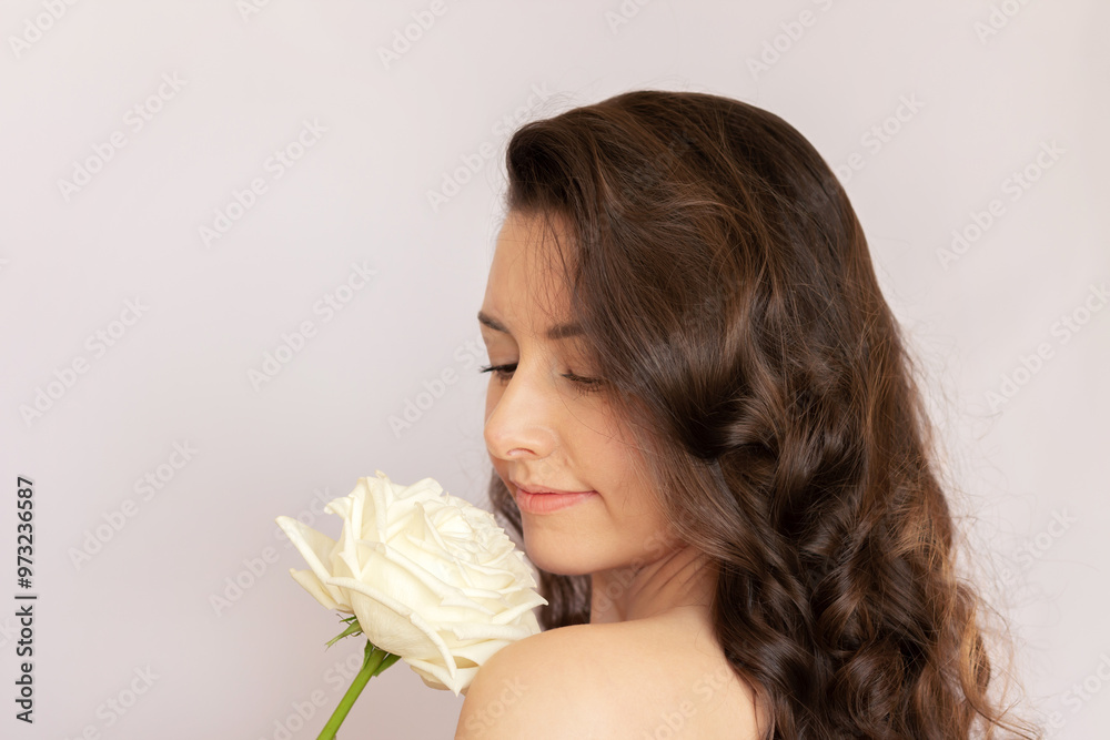 Young beautiful Caucasian brunette woman with curly hair smiles and with pleasure gently sniffs a white rose Young beautiful Caucasian brunette woman with curly hair smiles and with pleasure gently sniffs a white rose