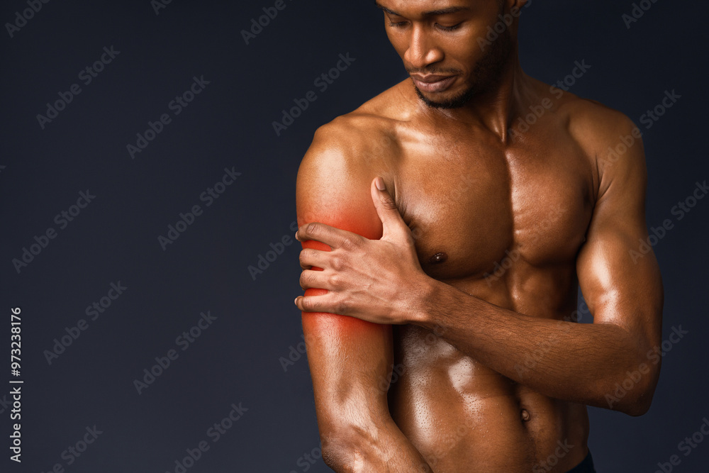 Fototapeta premium Pain In The Shoulder. Muscular black bodybuilder touching hand with red sore zone, sports injury, copyspace