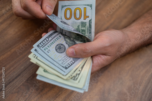 Hands counting US dollar banknotes on a wooden surface. Cash handling and financial management concept. Perfect for themes of personal finance, budgeting, and economic transactions 