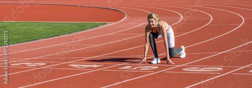 Girl is trained at the beautiful stadium. Female runner training in summer day outdoors on the stadium. Runner woman in sportswear getting ready to run sprint at low start on stadium track