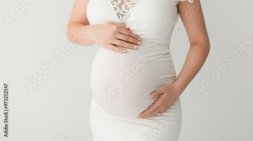 close up of woman holding her pregnant belly, dressed in white dress, similar to a wedding dress