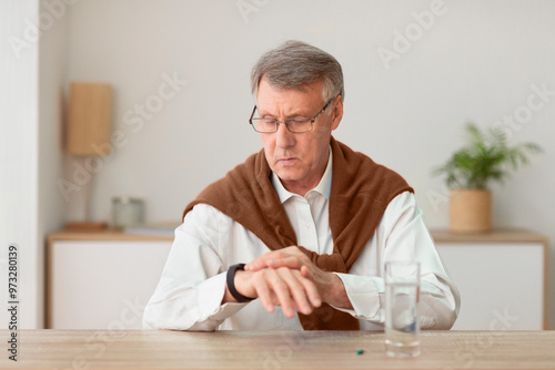 Medical Treatment. Serious Senior Gentleman Taking A Pill Checking Time With Smartwatch Sitting At Desk Indoor