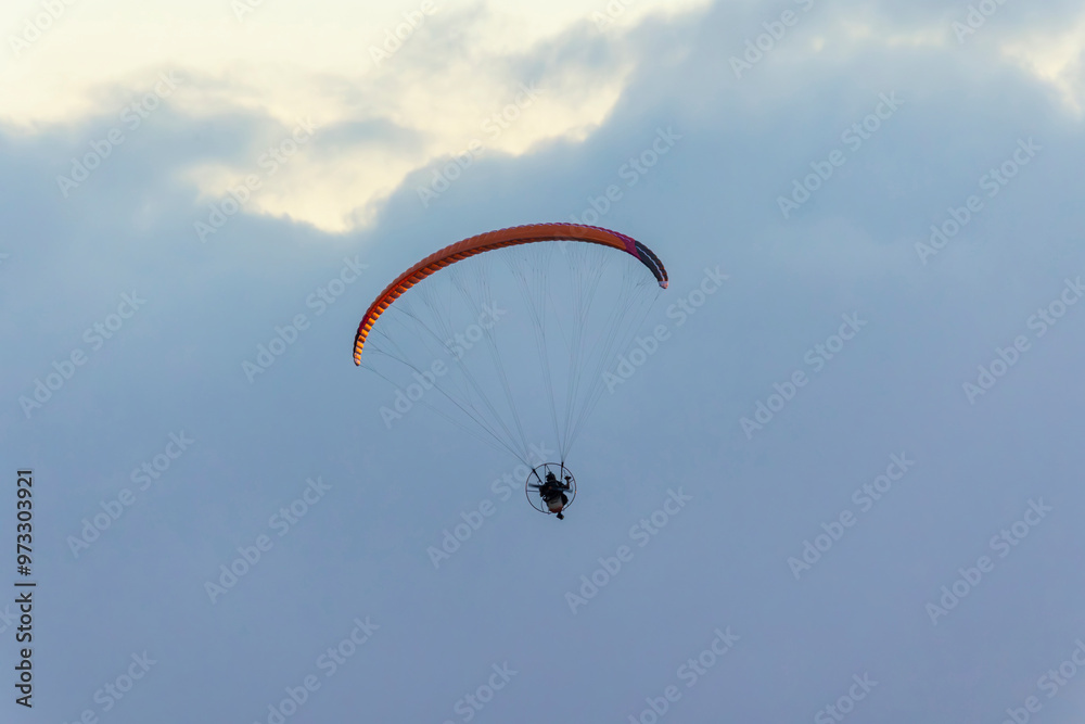 Paraglider free flying in harness with propeller motor and colorful fabric wing in blue sky Paraglider free flying in harness with propeller motor and colorful fabric wing in blue sky