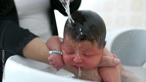 Newborn baby being lovingly cradled in a bath, with a hand gently resting on the baby's head for comfort and reassurance. baby's peaceful expression photo