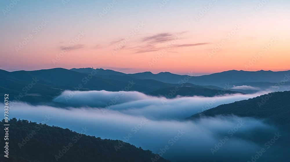 Fototapeta premium Early morning mist envelops the mountains as the sun rises over the landscape at dawn