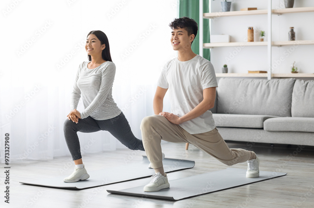 Obraz premium Motivated asian young couple exercising together at home, positive korean man and woman in sportswear standing on fitness mat, stretching and smiling, copy space. Healthy lifestyle concept