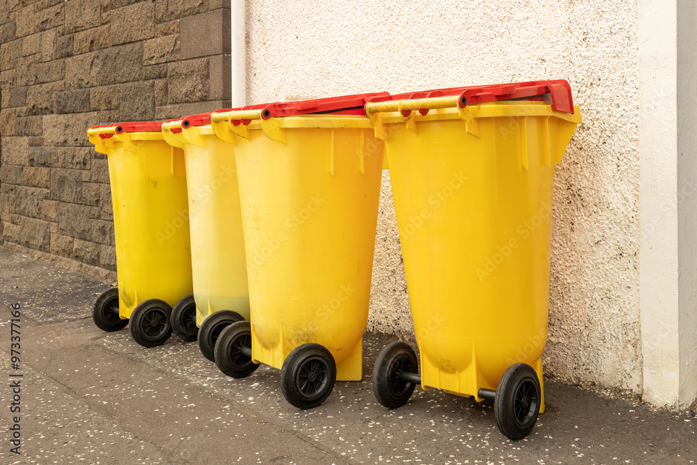 Used Cooking Oil Recycling: Yellow plastic wheelie wheeled bins with red lids outside restaurant kitchen on kerbside pavement Used Cooking Oil Recycling: Yellow plastic wheelie wheeled bins with red lids outside restaurant kitchen on kerbside pavement