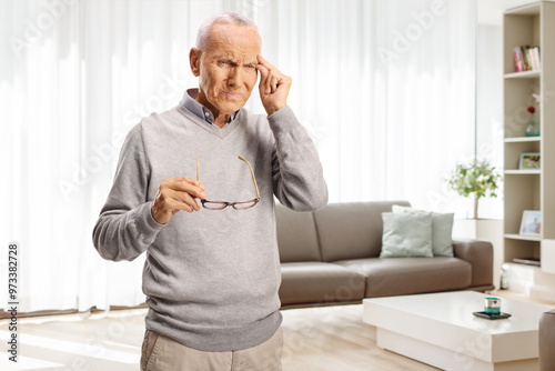 Elderly man with headache holding his forhead at home photo