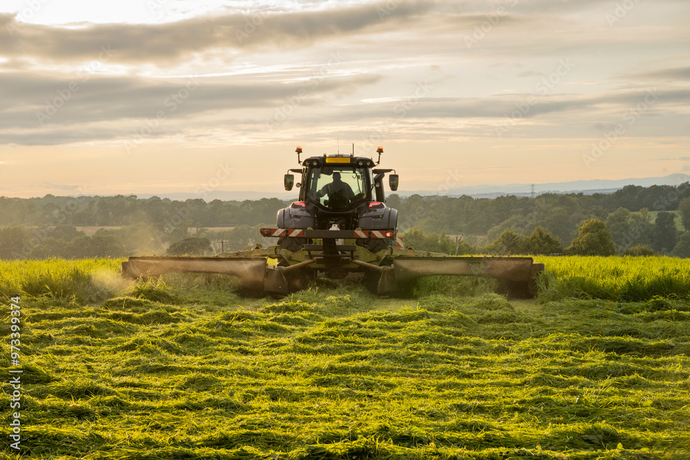 Farm tractor and mower cutting hay field at sunset in Scottish farmland Farm tractor and mower cutting hay field at sunset in Scottish farmland