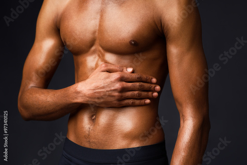 Bodybuilding Concept. Strong athletic afro man with muscular naked torso touching his body over black studio wall