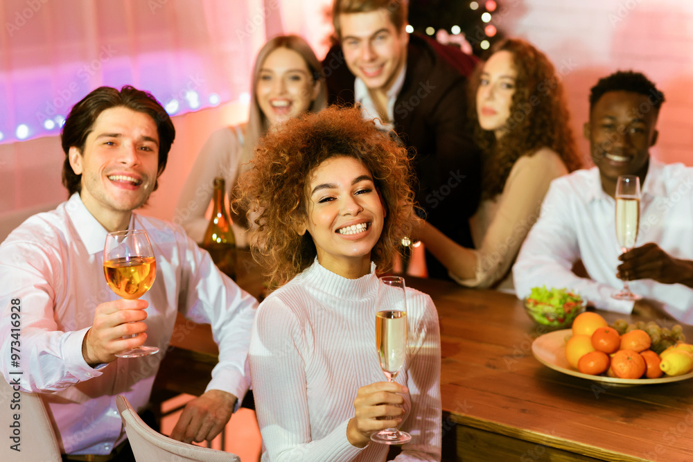 Cheers, Merry Christmas. Friends Holding Glasses Toasting Celebrating Xmas Sitting At Table Indoors, Smiling To Camera. Cheers, Merry Christmas. Friends Holding Glasses Toasting Celebrating Xmas Sitting At Table Indoors, Smiling To Camera.