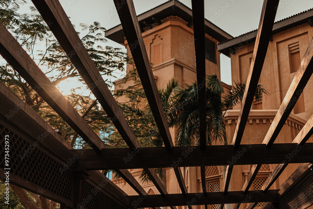 Obraz premium Sunlight shining through wooden pergola near traditional Arabic architecture