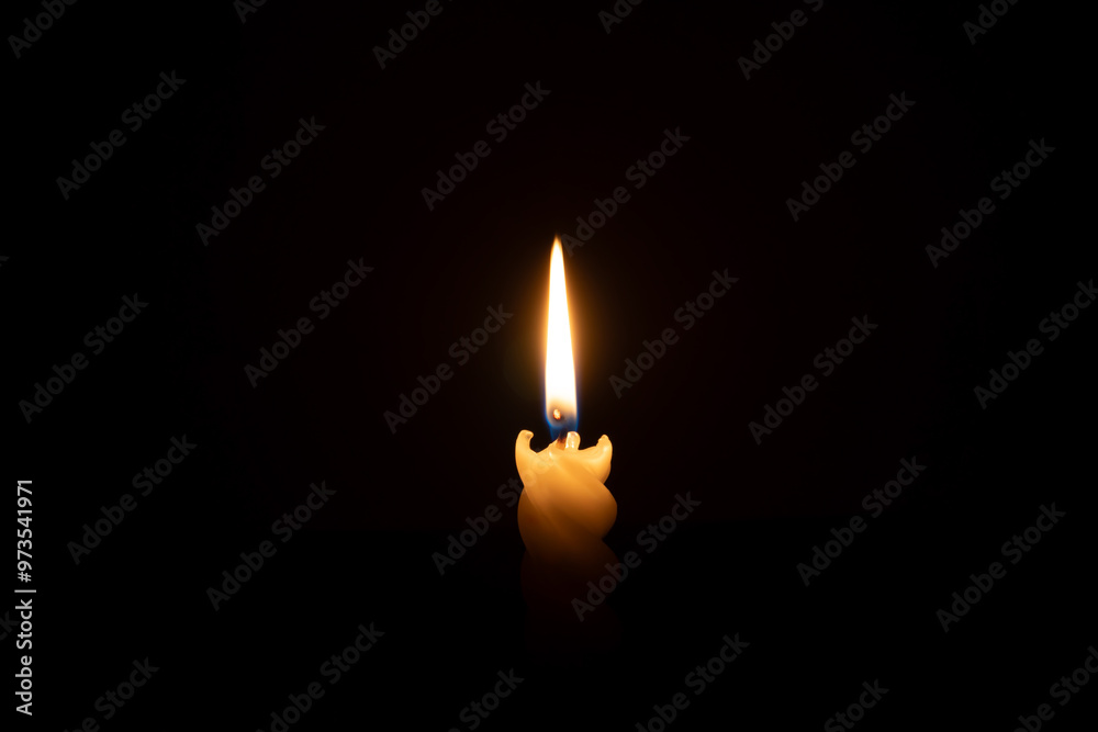 A single burning candle flame or light glowing on a spiral white candle on black or dark background on table in church for Christmas, funeral or memorial service with copy space A single burning candle flame or light glowing on a spiral white candle on black or dark background on table in church for Christmas, funeral or memorial service with copy space