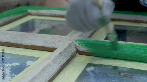 Wooden window painted green wearing gloves. Applied with brush. Patch of old wooden surface, showing through cracked and flaking paint. Handiwork, restore woodwork outdoor
