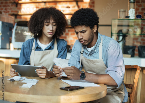 Problems in small business during covid-19 lockdown. Sad millennial african american couple owners in aprons work with accounts, and solve debt problems bookkeeping in cafe, empty space photo