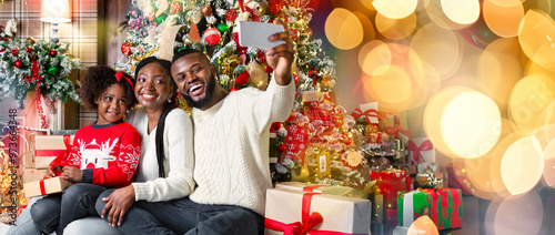 Slika na platnu Happy african american family of three taking selfie near Christmas tree at home