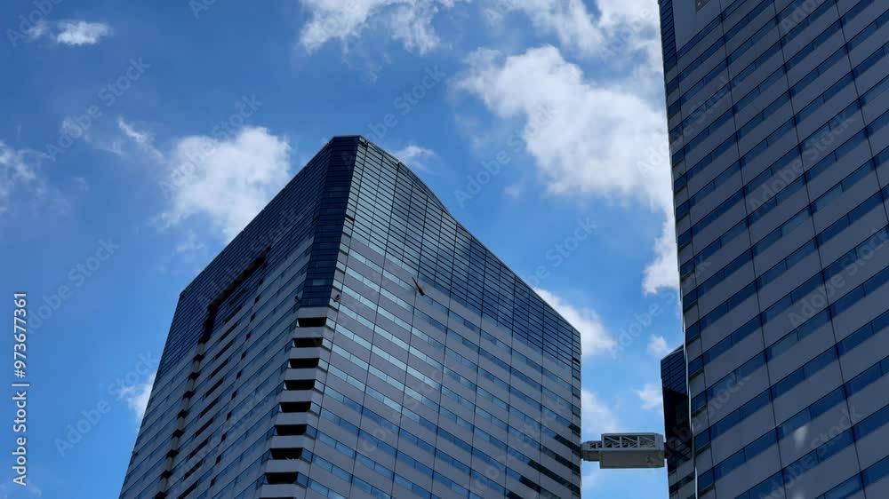 Modern skyscrapers with reflective glass windows against a blue sky and scattered clouds Modern skyscrapers with reflective glass windows against a blue sky and scattered clouds