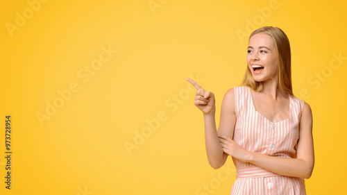 Great offer. Joyful young woman in summer dress pointing aside at copy space on yellow background, demonstrating cool promo