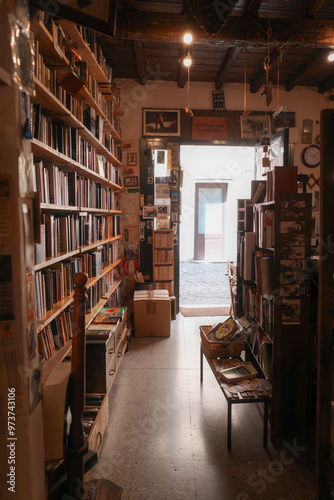 Obraz na płótnie A cozy bookstore with wooden shelves filled with books, a small bench, and an open door that provides a view of the outside, giving a warm and inviting atmosphere