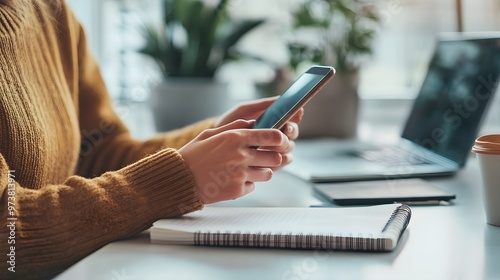 Close-up of Woman's Hands Using Smartphone with Laptop and Notebook in Background