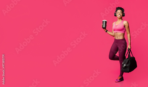 Excited african fitness girl with earphones, bag and shaker going to gym, red background photo