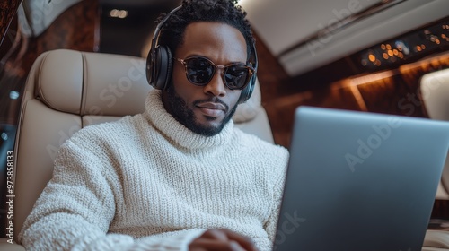Affluent Black man in a white sweater and headphones working on a laptop inside a private jet, high-resolution photograph capturing a luxurious and stylish scene.

