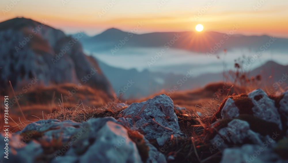 Obraz premium Serene mountain landscape at sunrise, with soft warm light bathing foreground rocks and grass