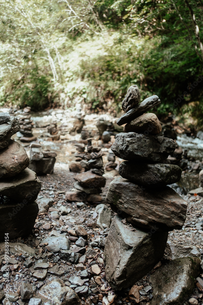 Stacked stones in a serene wooded area near a gentle stream, showcasing nature's tranquility and human creativity on a sunny day Stacked stones in a serene wooded area near a gentle stream, showcasing nature's tranquility and human creativity on a sunny day