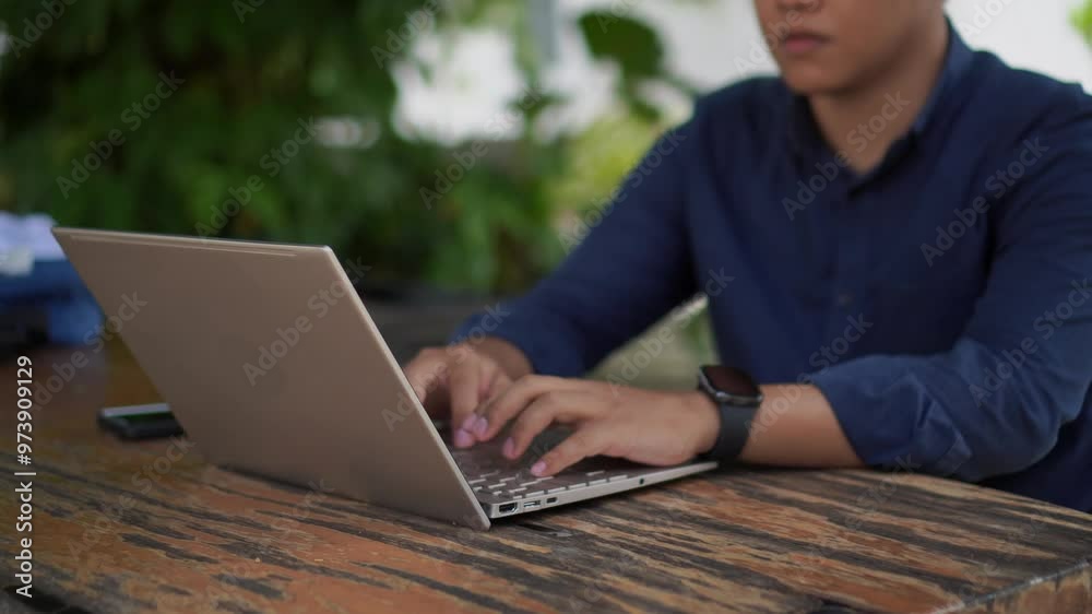 A man with blue shirt working on his laptop at the outdoor cafe. Man focused and concentrated to his laptop. A man with blue shirt working on his laptop at the outdoor cafe. Man focused and concentrated to his laptop.