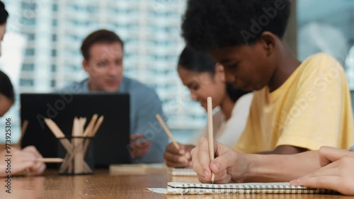 Closeup of student hand taking a note while girl ask teacher a question. Diverse student learning and study with smart happy instructor in classroom. Focus on hand. Creative education. Edification photo