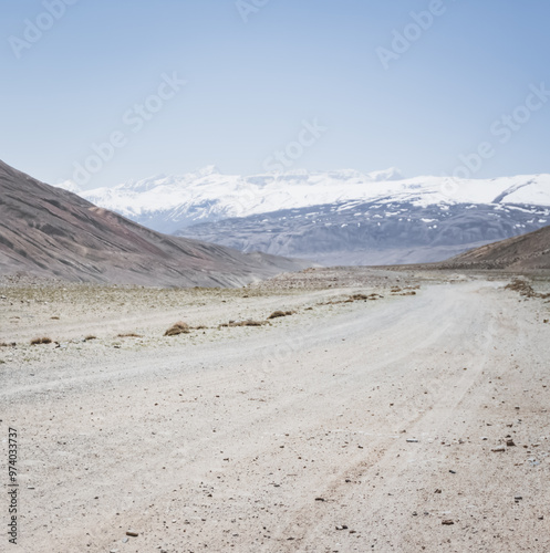 Dusty road of the Pamir Highway winds and twists in the valley of the Tien Shan Mountains against the backdrop of a mountain range with snow in Tajikistan in the Pamirs, landscape for the background photo