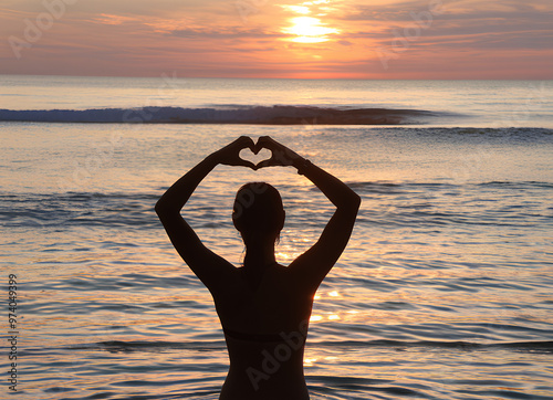 A young woman at the beach making a heart shape sign using her hands against the backdrop of a sun