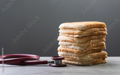 Slices of bread stacked together with a red stethoscope on a gray wooden table against a dark gray background. The image conveys the concept of the relationship between diet and health. photo