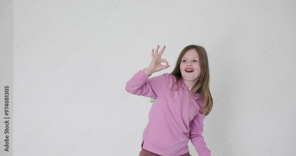 Charming little girl smiles and shows OK sign with fingers on white background. Eyes of long-haired child sparkle with happiness and confidence Charming little girl smiles and shows OK sign with fingers on white background. Eyes of long-haired child sparkle with happiness and confidence