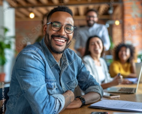 A man smiles at the camera while sitting with his team. AI.