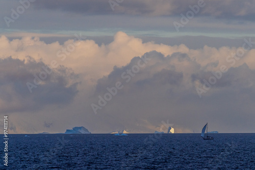 An Antarctic landscape, taken during the golden hour, just after sunrise, in the Gerlache Strait. A little sailboat in the foreground explores the Antarctic waters. photo