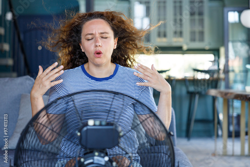 Young woman trying to cool off in front of an electric fan at home