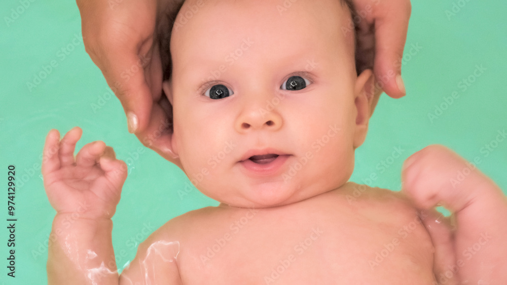 Mother teaches a newborn baby to swim and stay on the water. Two-month-old baby is bathing in a large bathtub. Newborn baby is in the water, bathroom. Hygiene procedures of a newborn baby Mother teaches a newborn baby to swim and stay on the water. Two-month-old baby is bathing in a large bathtub. Newborn baby is in the water, bathroom. Hygiene procedures of a newborn baby