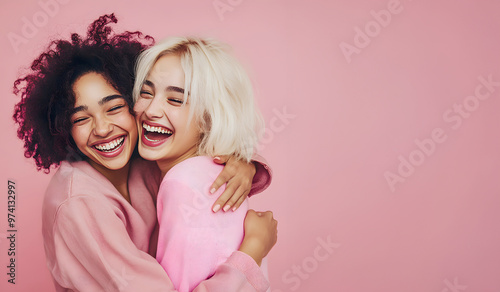 Two young women are having fun and friends are hug over pink background