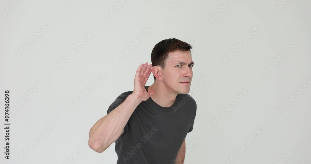 Curious man strains to hear faint sound on white background. Male in grey t-shirt tries to discern quiet conversation of coworkers to hear secret Curious man strains to hear faint sound on white background. Male in grey t-shirt tries to discern quiet conversation of coworkers to hear secret