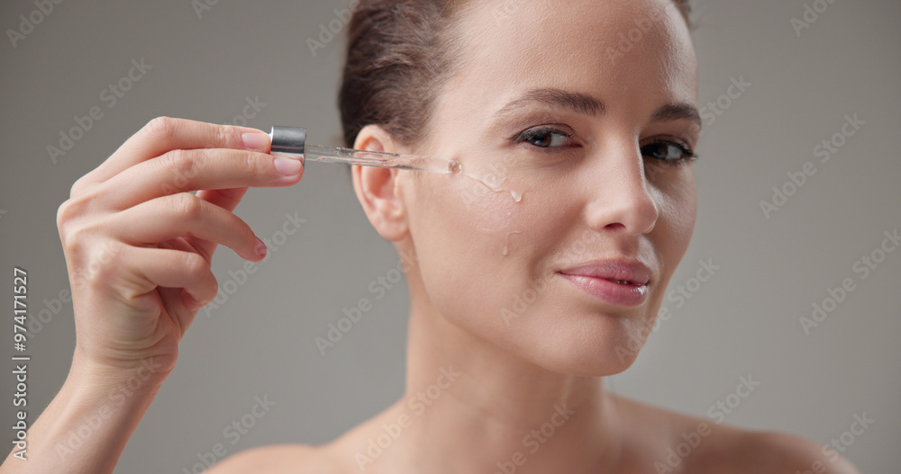 Obraz premium Beauty, health, cosmetics, anti-aging therapy and skin care concept - young beautiful brunette Caucasian woman applying cosmetic serum from a pipette for facial skin care