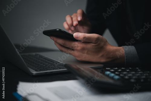 Businessman using smartphone and laptop for financial calculations and online transactions