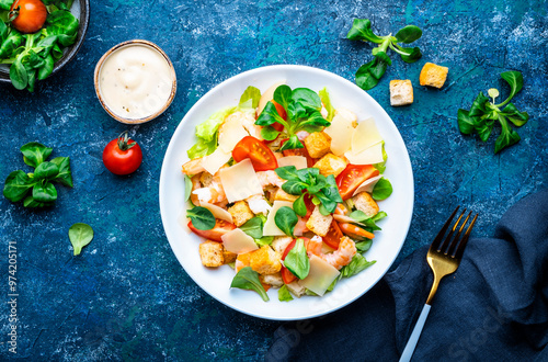 Caesar salad with shrimp, tomatoes, iceberg lettuce, croutons, parmesan cheese and classic dressing. Blue background, top view