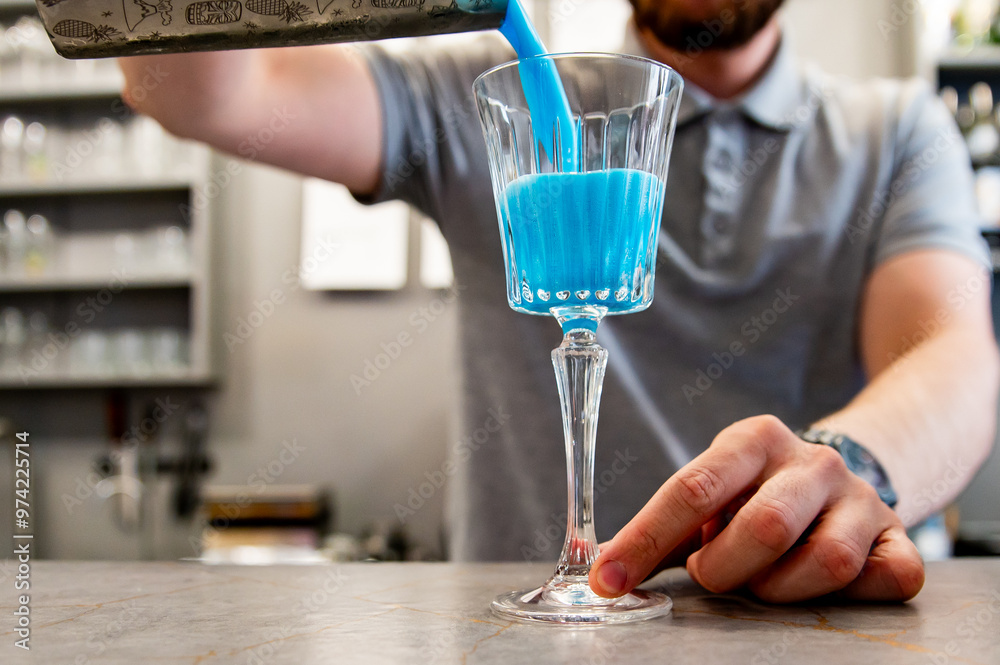 A bartender pours a vibrant blue cocktail into a glass on a bar counter, capturing the dynamic motion of the liquid. The scene is set in a stylish bar environment, emphasizing the elegance drink. A bartender pours a vibrant blue cocktail into a glass on a bar counter, capturing the dynamic motion of the liquid. The scene is set in a stylish bar environment, emphasizing the elegance drink.