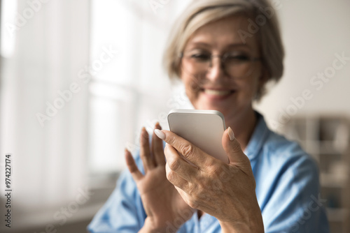 Close up cropped view smiling middle-aged woman looking at her smartphone, texting or chatting with family or friend, sharing messages, browsing social media networks, comfort and modern connectivity