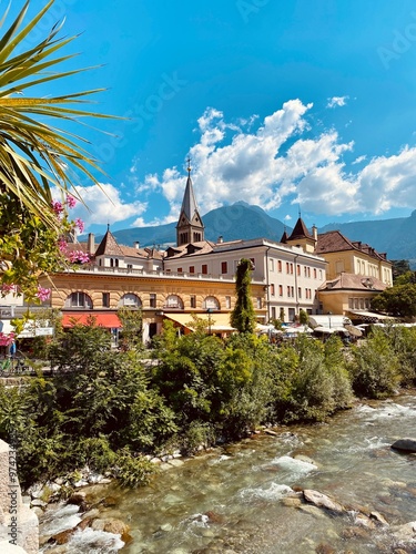 A picturesque view of the Passirio River flowing through Merano, South Tyrol. The image captures the serene beauty of the river, surrounded by lush greenery and charming architecture. photo