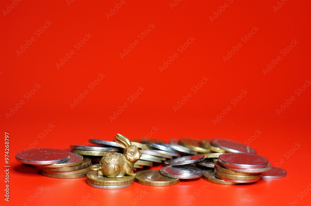 Naklejka premium A metal rabbit figurine with coins on a red background.