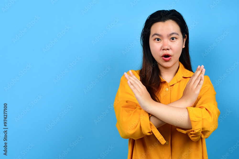 Beautiful Asian woman wearing orange or yellow shirt with hand gesture pose rejection or prohibition with copy space isolated blue backround Beautiful Asian woman wearing orange or yellow shirt with hand gesture pose rejection or prohibition with copy space isolated blue backround